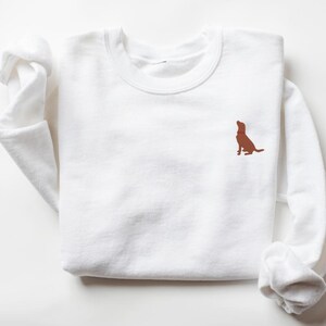 May include: White long-sleeved sweatshirt with a brown dog silhouette embroidered on the left chest.