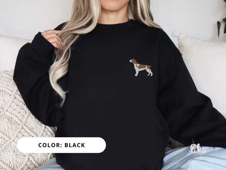 May include: Black sweatshirt with a brown and white dog silhouette embroidered on the left chest. The text "COLOR: BLACK" is displayed below the image.