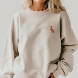 May include: A beige sweatshirt with a small, red embroidered dog silhouette on the front.