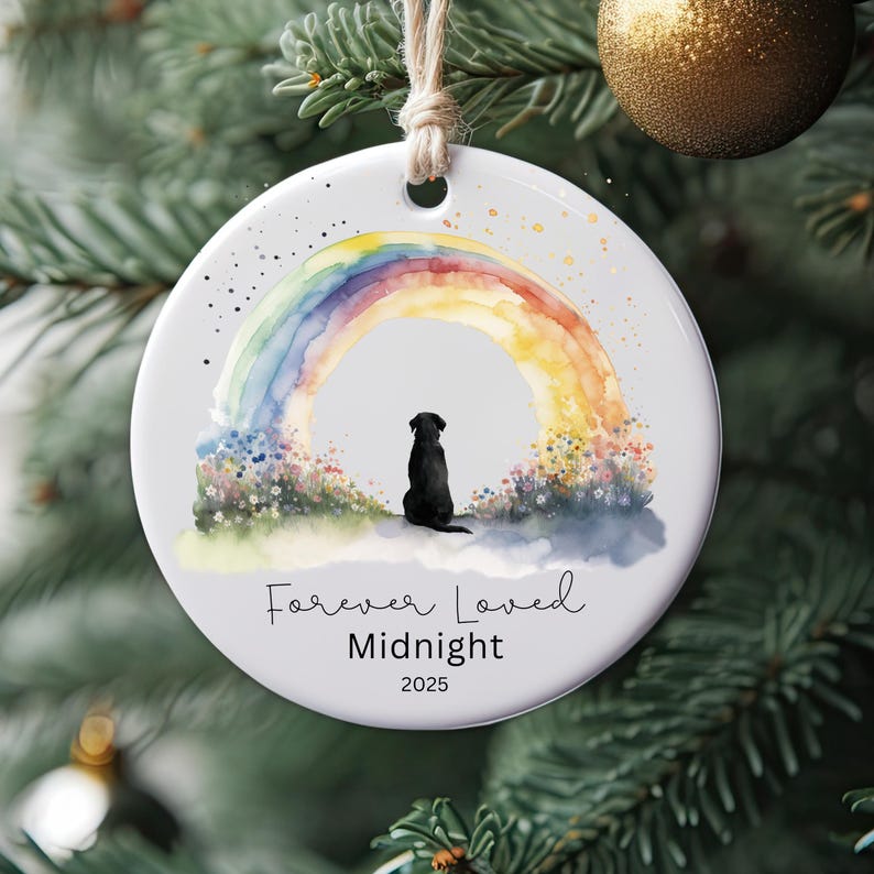 May include: Round white ceramic Christmas ornament featuring a watercolor rainbow and a black dog silhouette. The text "Forever Loved Midnight 2025" is written below the image. A jute string is attached for hanging.