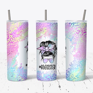 May include: A stainless steel tumbler with a white background and a colorful design featuring a woman with a messy bun, sunglasses, and a bow. The text "#BIGSISTER" is printed on the tumbler.