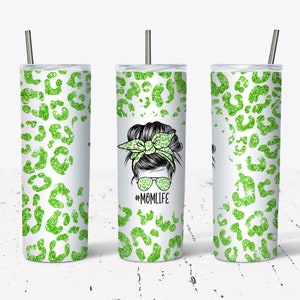 May include: A white tumbler with a green glitter leopard print design. The tumbler features a graphic of a woman with a messy bun, sunglasses, and a headband, with the text #MOMLIFE. Includes a silver straw.