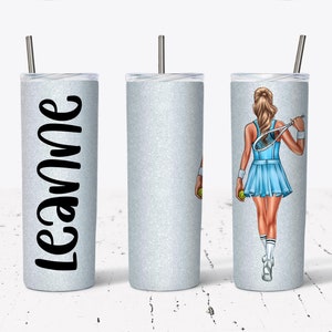 May include: A glittery silver tumbler with a stainless steel straw. One side features the name "Leanne" in black script. The other side displays a tennis player in a blue dress, holding a tennis racket and ball. A stylish and personalized gift.