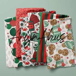 May include: Several folded fabrics featuring festive Christmas patterns. Designs include baubles, floral arrangements, post boxes, candy canes, cookies, and striped patterns in red, green, and white. The text "Angie Hughes" is visible across the fabrics.