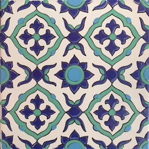 Może przedstawiać: Biała płytka ceramiczna z powtarzającym się wzorem niebieskich i zielonych wzorów kwiatowych. Płytka ma tradycyjny marokański styl.