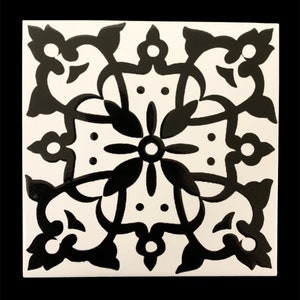 May include: Black and white ceramic tile with a geometric pattern. The pattern features a central flower with four petals and four smaller flowers in the corners. The tile has a glossy finish.