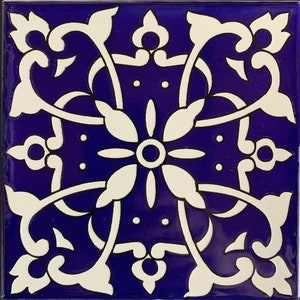 May include: A square tile with a white floral design on a deep blue background. The design features intricate swirls and a central flower with a circle in the middle.