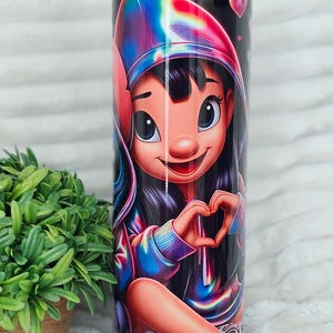 May include: A tall, cylindrical tumbler featuring a cartoon character in a colorful hoodie making a heart shape with their hands. The design includes vibrant rainbow hues and small pink hearts against a black background. A clear straw is visible.