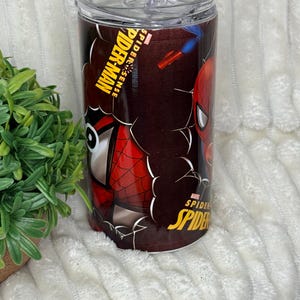 May include: A stainless steel tumbler with Spider-Man graphics. The design includes the words "Spider-Man" and "Spider-Sense" in yellow and white, along with images of the superhero. The tumbler has a clear lid.