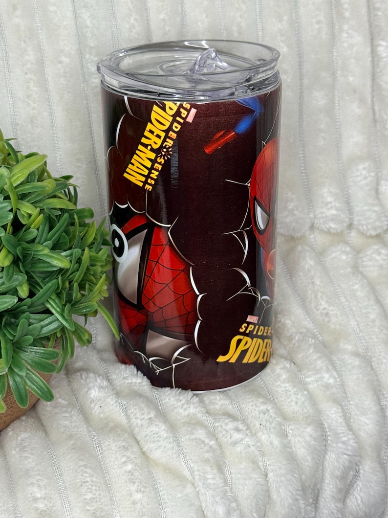 May include: A stainless steel tumbler with Spider-Man graphics. The design includes the words "Spider-Man" and "Spider-Sense" in yellow and white, along with images of the superhero. The tumbler has a clear lid.
