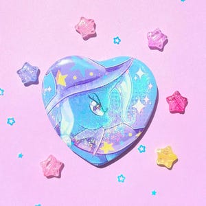 May include: A heart-shaped button featuring a blue and purple illustration of a pony with a star-studded design. The button is surrounded by star-shaped and star-shaped confetti on a pink background.