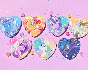 Puede incluir: Una colección de botones en forma de corazón con ilustraciones coloridas de personajes de dibujos animados. Los botones tienen un acabado brillante y están decorados con estrellas y purpurina. El fondo es de color lila claro.