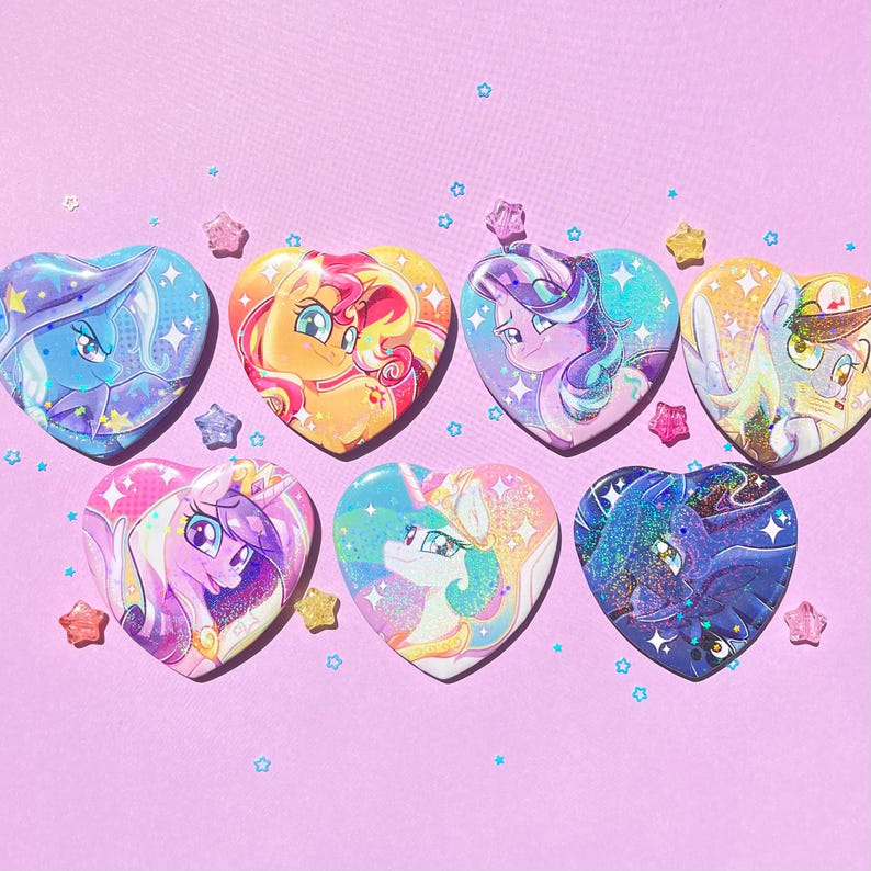 May include: A collection of heart-shaped buttons featuring colorful illustrations of cartoon characters. The buttons have a glossy finish and are decorated with stars and glitter. The background is a light purple color.
