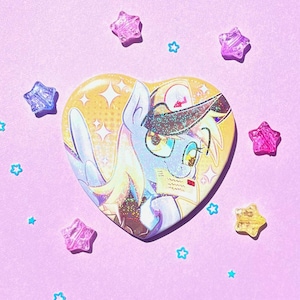 May include: A heart-shaped button featuring a cartoon pony with a yellow and blue color scheme. The pony has a hat and glasses. The background is yellow with white stars. Surrounding the button are star-shaped and star-shaped confetti.