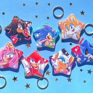 Op de afbeelding: Een verzameling stervormige karakterspelden met Sonic the Hedgehog en vrienden. Elke speld toont een ander personage in levendige kleuren, tegen een lichtblauwe achtergrond met gouden sterren en ringen.