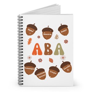 以下が含まれることがあります： 「ABA」という文字が大きくカラフルに書かれた白いスパイラルノート。文字の周りを囲むように、どんぐりがあり、「応用」「行動」「分析」「技術」「概念的に体系的」「効果的」「汎用性」といった言葉が書かれている。