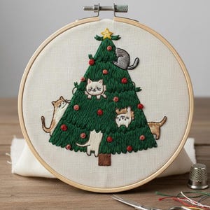 Pode incluir: Bordado de árvore de Natal verde com enfeites vermelhos e uma estrela dourada, com gatos. A obra está emoldurada em um círculo de madeira. Uma decoração de Natal original e artesanal.