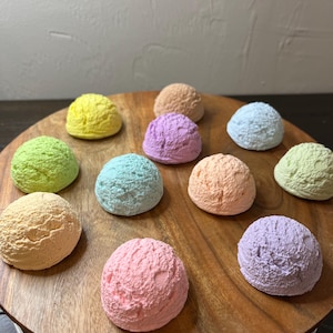 May include: A wooden tray with ten colorful ice cream scoops in various pastel shades, including pink, blue, green, yellow, and purple.