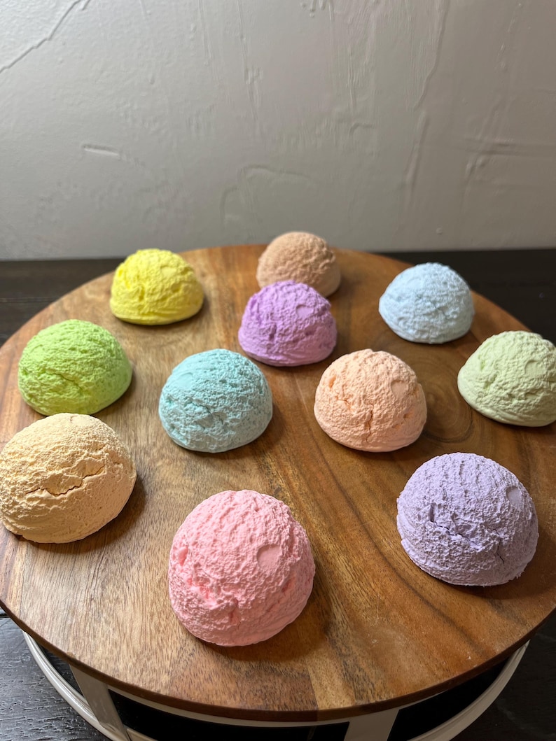 May include: A wooden tray with ten colorful ice cream scoops in various pastel shades, including pink, blue, green, yellow, and purple.