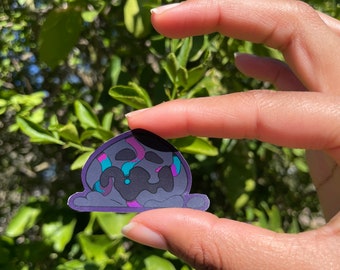 May include: A sticker of a cartoon ghost with a black, purple, pink, and blue design. The ghost is melting and has a sad expression.