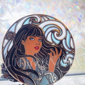 Peut inclure: Épingle émaillée circulaire représentant une femme aux longs cheveux noirs et aux yeux bleus. La femme est entourée d'un motif tourbillonnant bleu et blanc. L'épingle a une bordure dorée et un style d'illustration détaillé.