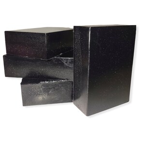 May include: A collection of six rectangular, black bars with a slightly textured surface. The bars are stacked and arranged, with one standing upright. The overall appearance suggests a soap or a similar solid product.