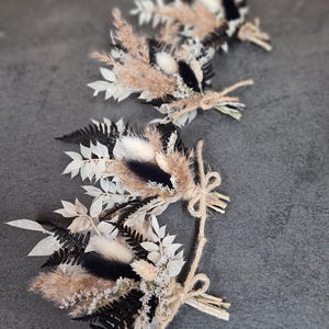May include: Three small floral arrangements featuring dried black ferns, white leaves, tan pampas grass, and fluffy white bunny tails. Each bundle is tied with a natural jute twine bow, creating a cohesive set of decorative botanical accents.