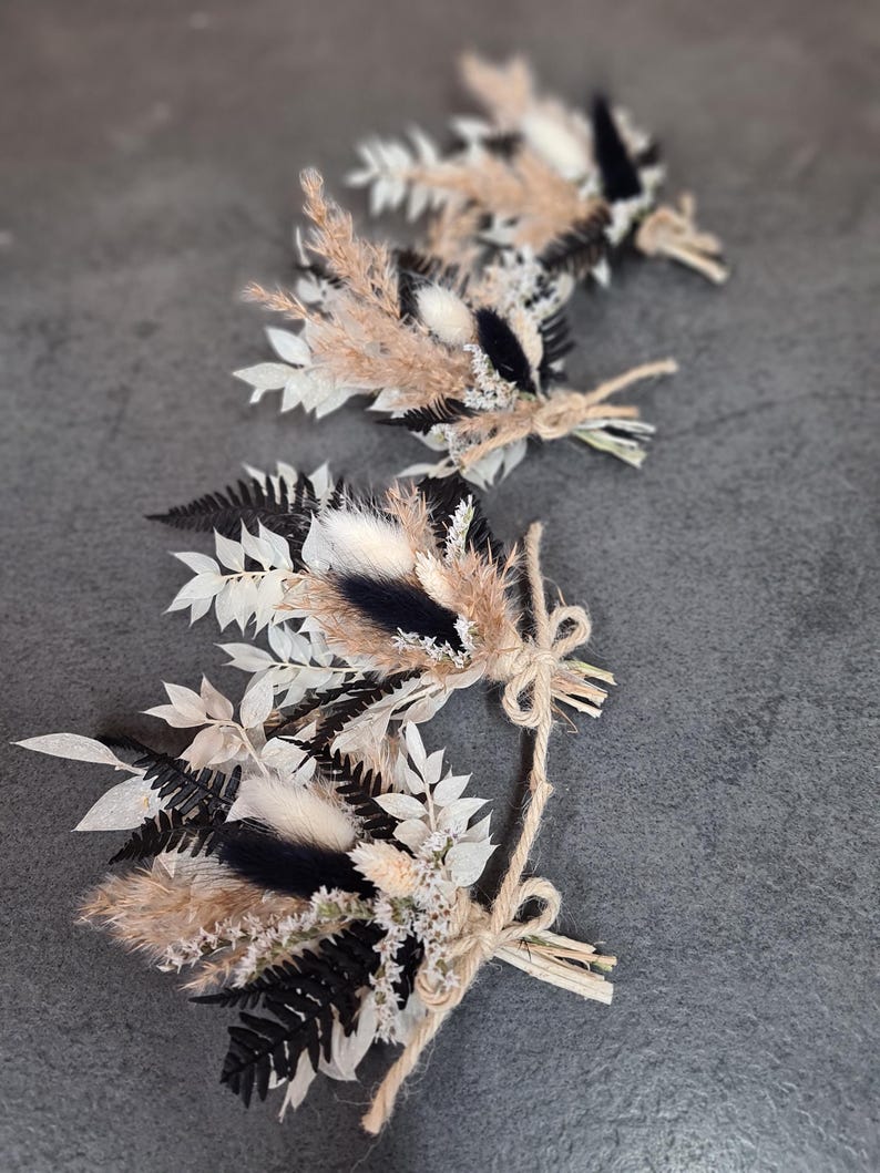 May include: Three small floral arrangements featuring dried black ferns, white leaves, tan pampas grass, and fluffy white bunny tails. Each bundle is tied with a natural jute twine bow, creating a cohesive set of decorative botanical accents.