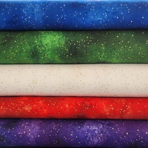 May include: A stack of colorful fabric rolls. The fabrics are in shades of blue, green, white, red, and purple. Each fabric has a speckled pattern of small, gold-colored dots, creating a starry night effect. The fabrics are neatly stacked.