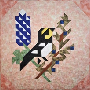 May include: A quilt block featuring a black and white bird with a yellow beak, a blue and white flower, and a brown and green branch with small blue berries.