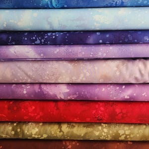 May include: A stack of eight fabric swatches with a splatter paint design. The colors are blue, light blue, purple, lavender, pink, red, brown, and beige.