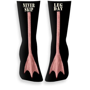 May include: Black socks featuring a pink duck foot design. The socks display the words "NEVER SKIP" and "LEG DAY" in white. The duck feet have red toenails.