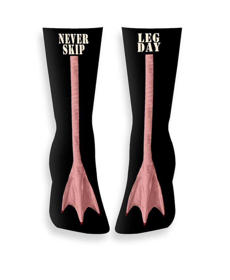 May include: Black socks featuring a pink duck foot design. The socks display the words "NEVER SKIP" and "LEG DAY" in white. The duck feet have red toenails.