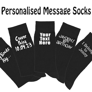 Può includere: Cinque paia di calzini neri con testo bianco. I calzini hanno messaggi diversi, tra cui "Big Socks Big...", "Connor Ibiza 10.04.23", "Your Text Here", "Jayden's 18th Birthday" e "I Belong to Jenny".