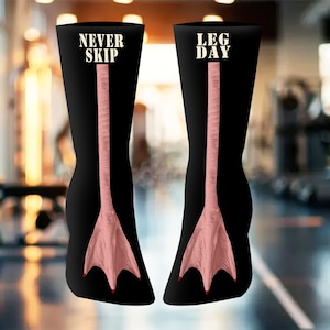 Könnte beinhalten: Schwarze Kniestrümpfe mit einem rosa Entenfuß-Design. Auf einem Strumpf steht "NEVER SKIP" und auf dem anderen "LEG DAY" in weißer Schrift. Die Socken zeigen eine detaillierte Illustration eines Entenfußes.