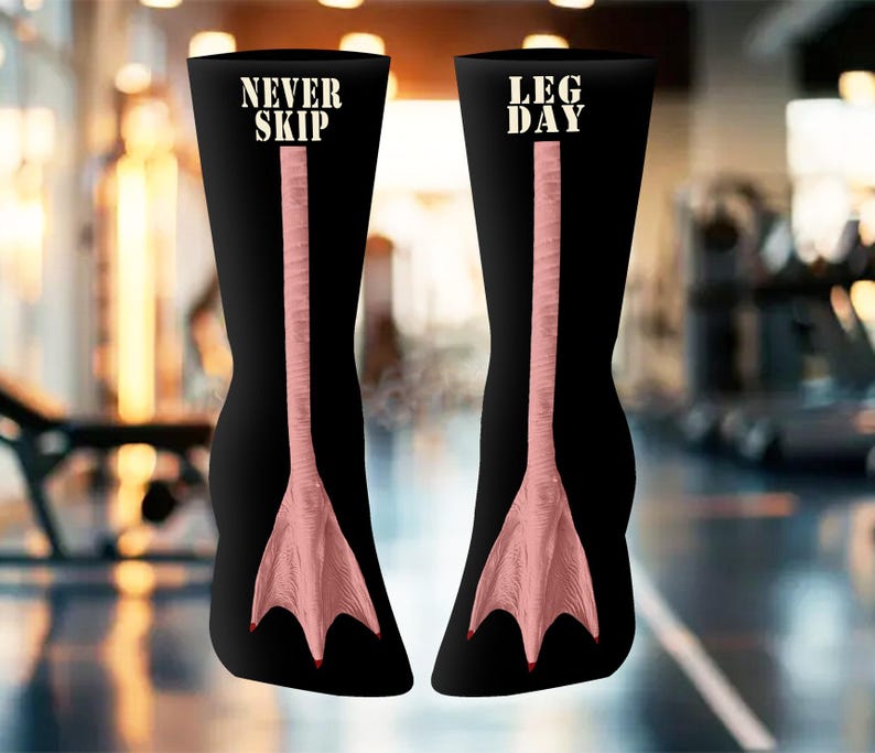 May include: Black knee-high socks with a pink duck foot design. One sock has "NEVER SKIP" and the other "LEG DAY" in white text. The socks feature a detailed illustration of a duck's foot, ideal for gym enthusiasts.