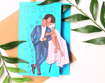 May include: A blue and white card with the text "It's Our Anniversary" and a cartoon illustration of a couple. The woman is wearing a pink dress and the man is wearing a blue suit. The card is on a brown background.