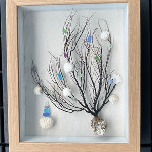 May include: A framed shadow box art piece featuring a dried sea branch with white seashells and colorful glass beads. The branch is displayed on a white canvas background.