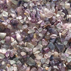 Könnte beinhalten: Nahaufnahme einer Sammlung kleiner, getrommelter Amethyststeine. Die Steine sind in verschiedenen Schattierungen von Lila, Lavendel und Klar, wobei einige einen Hauch von Grün zeigen. Die Steine sind in einem zufälligen Muster angeordnet, was eine schöne und natürliche Textur erzeugt.