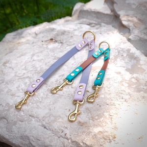 Op de afbeelding: Een drievoudige hondenriem met een lavendel, turquoise en bruin lederen ontwerp. De riem heeft gouden hardware en drie clips.