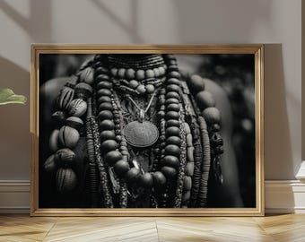 Op de afbeelding: Zwart-wit ingelijste print met een close-up van gelaagde kralenkettingen en versieringen. De kettingen bevatten kralen van verschillende maten en vormen, met een centrale hanger. De afbeelding staat in een goudkleurige lijst.