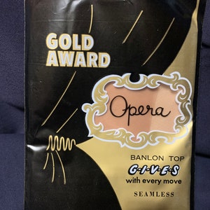 May include: A gold and black package for Opera brand seamless pantyhose. The package features the words "Gold Award" and "Opera" in a gold script font. The text "Banlon Top Gives with every move Seamless" is also printed on the package.