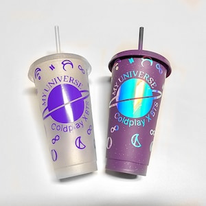 May include: Two reusable tumblers with lids and straws. The tumblers are decorated with a purple and silver holographic design that says "My Universe Coldplay x BTS". One tumbler is silver and the other is purple.