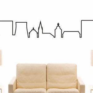 May include: A black and white line art illustration of the Hürth skyline. The illustration is on a white wall with a couch and two lamps in the foreground.