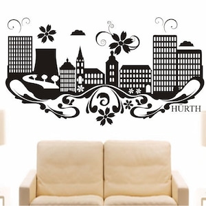May include: Black and white silhouette wall decal of a city skyline with stylized flowers and swirls. The decal includes the word "Hürth".