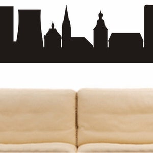 May include: Black and white silhouette of the city skyline of Hürth, Germany. The skyline features several buildings, including a church with a tall spire, a factory, and a few residential buildings.