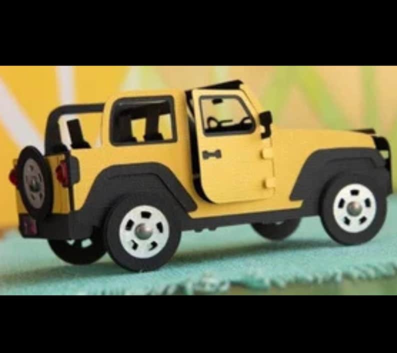 May include: A yellow and black toy off-road vehicle model featuring a spare tire mounted on the rear, black wheel arches, and a side door that is partially open. The vehicle has a boxy frame with visible interior details and white wheels.