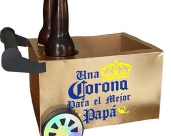 May include: A gold-colored beer cart with two brown beer bottles. The cart has a black handle and a wheel with a rainbow design. Text on the cart reads "Una Corona Para el Mejor Papá."