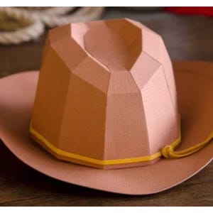 May include: A brown cowboy hat with a yellow band and a brown tassel. The hat is made of a textured material and has a geometric design.