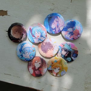 May include: A collection of nine round pinback buttons featuring colorful anime-style character illustrations. The buttons showcase various characters with vibrant hair and clothing, set against a white background.
